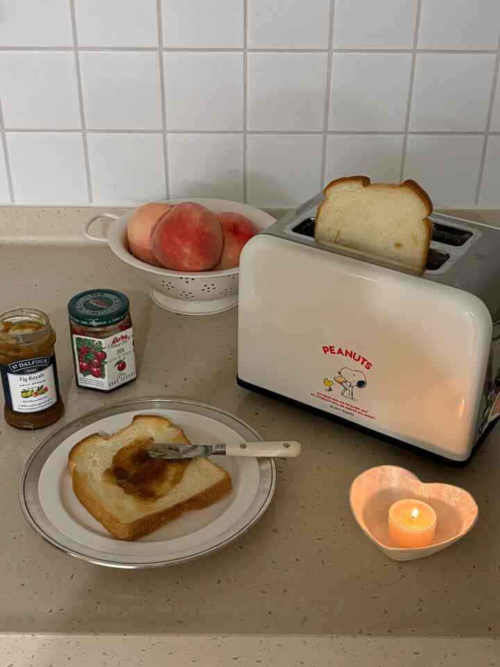 白いタイル壁とベージュのカウンターの家カフェ風キッチン、トースター、食パン、ジャム、桃が置かれた雰囲気ある空間