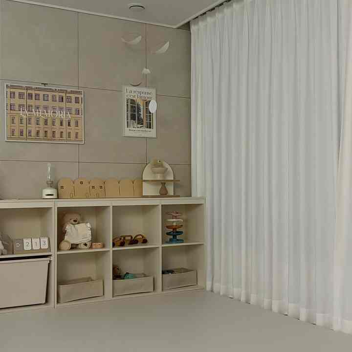 白とベージュの色調の子供部屋、整頓された収納棚と木製のおもちゃ、モビールが配置されたシンプルな印象的な空間