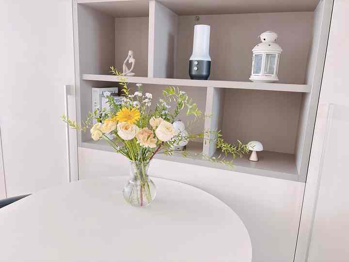 白を基調としたダイニングルーム、丸いダイニングテーブルの上に新鮮な花が飾られた花瓶が置かれた、清潔で明るい雰囲気のインテリア