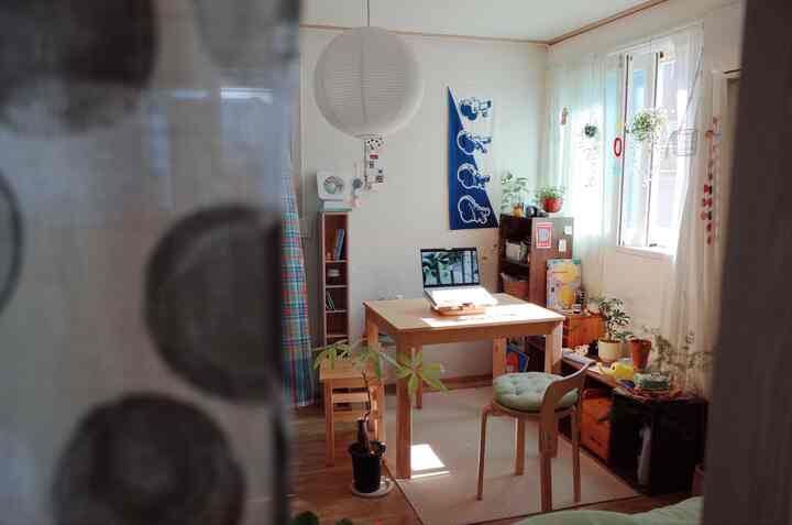 ナチュラルな木目調のワンルーム、木製のダイニングテーブルと椅子、本棚、植物が配置された落ち着いた雰囲気のあるインテリア