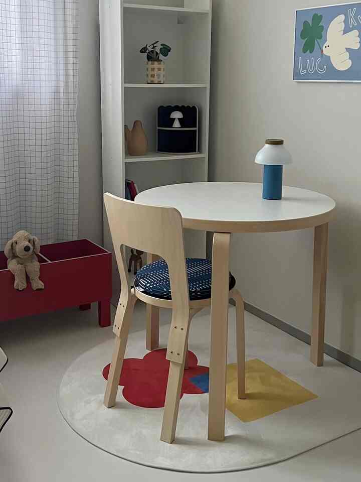 白とナチュラルトーンの子供部屋、丸テーブルと椅子、本棚とぬいぐるみが配置された印象的な空間