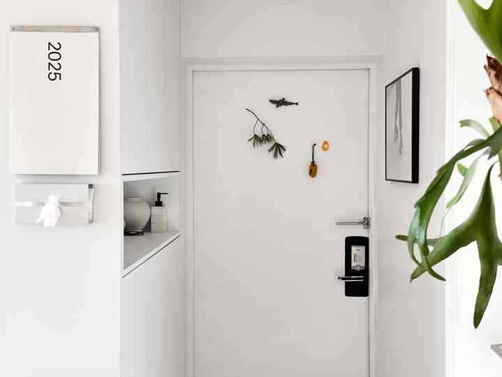 白を基調とした玄関、大きなシューズラックと2025年の壁掛けカレンダーが配置された清潔感のある収納スペース