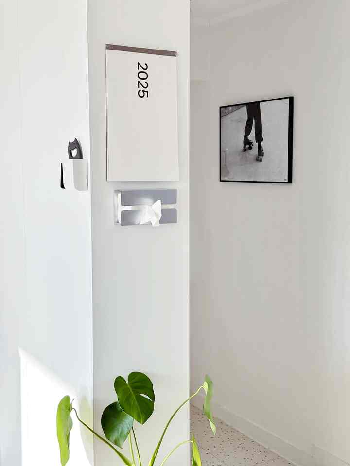 明るい白色調のワンルーム、左側にモンステラの植物とモノクロ写真の額縁が配置された清潔感のあるインテリア