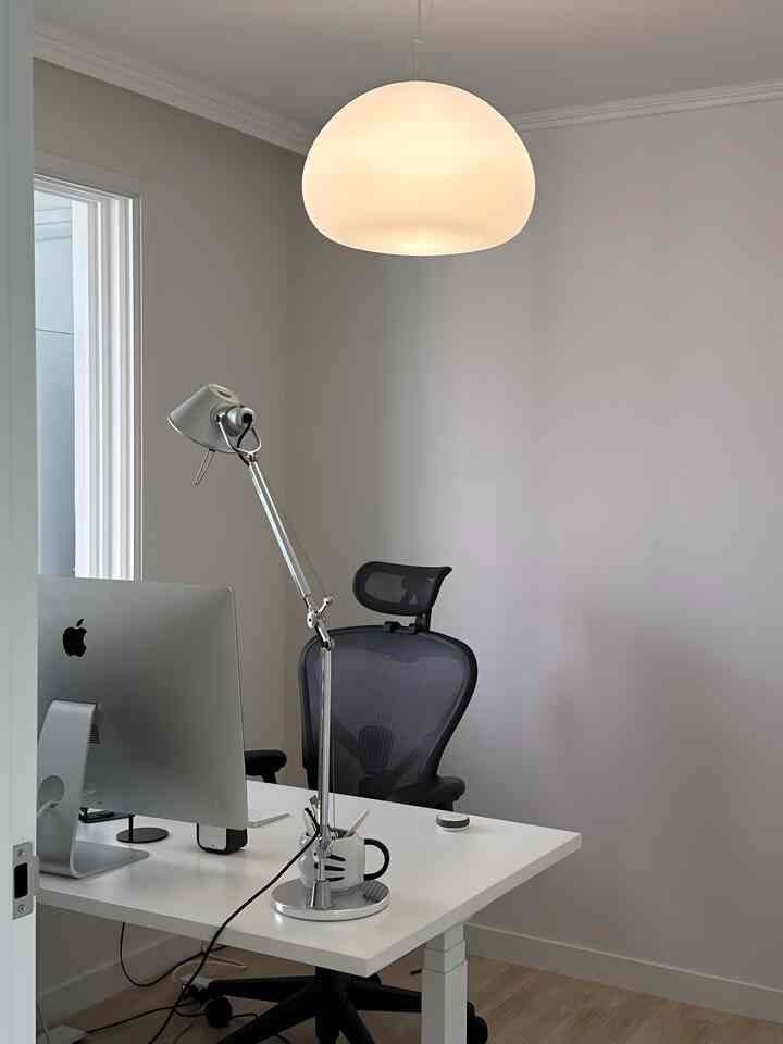 ホワイトとグレーのトーンのホームオフィス、機能的なオフィスチェアと昇降式デスクが配置されたモダンでシンプルな新婚ワークスペース