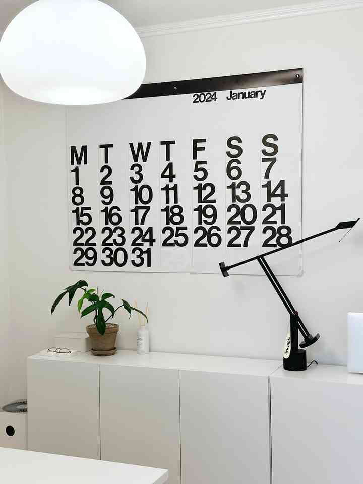 白と黒のコントラストが際立つ狭いホームオフィス、壁に大きなカレンダーと収納キャビネットが配置されたミニマルなインテリア