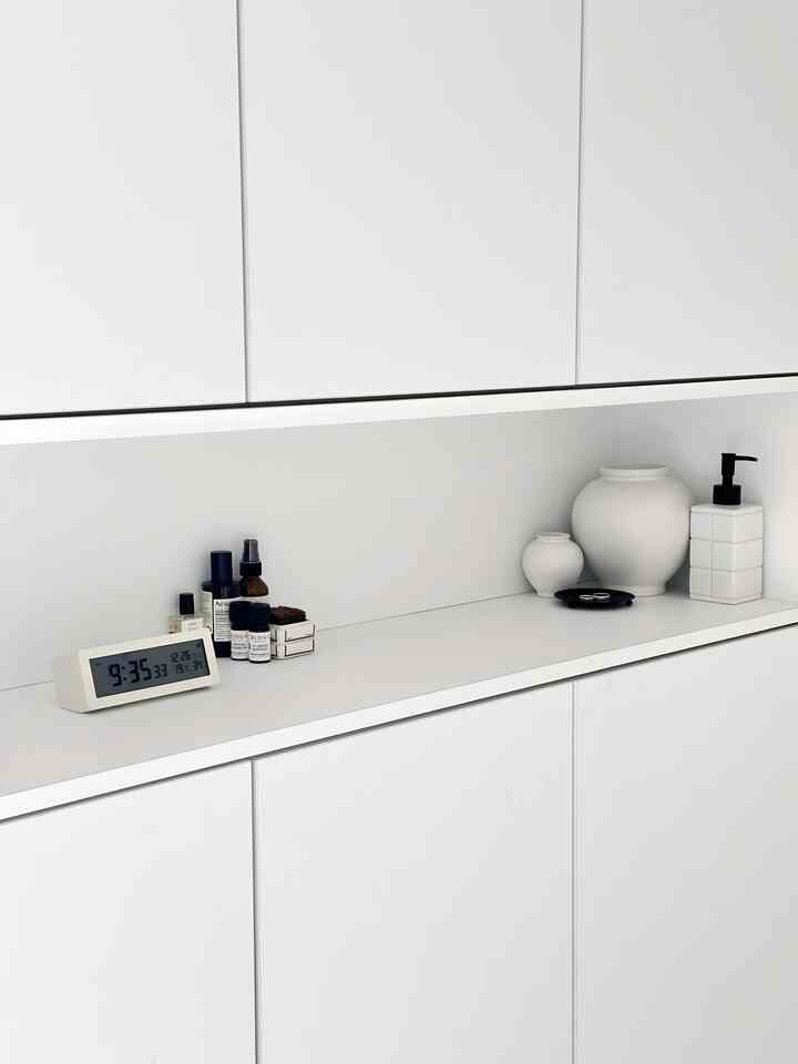 白を基調とした玄関スペース、シューズラックにデジタル時計、ディフューザー、マットな陶器のオブジェが整然と配置されたミニマルなインテリア