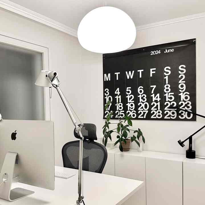白と黒のトーンが特徴のホームオフィス、机とオフィスチェア、大きな壁掛けカレンダーが配置された整った作業空間