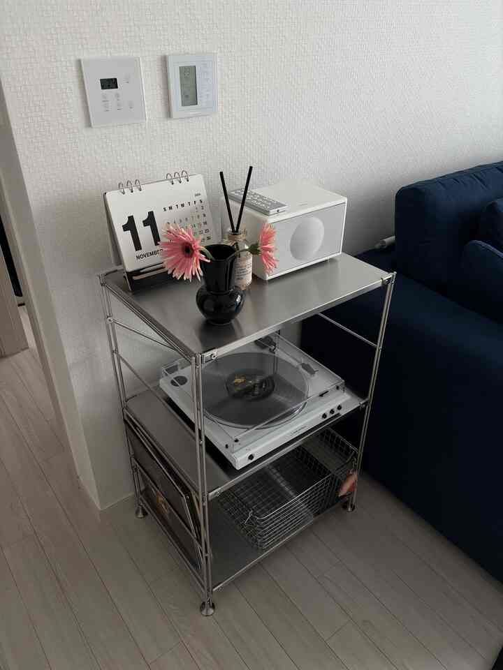 白い壁とメタル棚にオーディオシステムとターンテーブルが置かれたネイビーソファの隣のリビングルーム