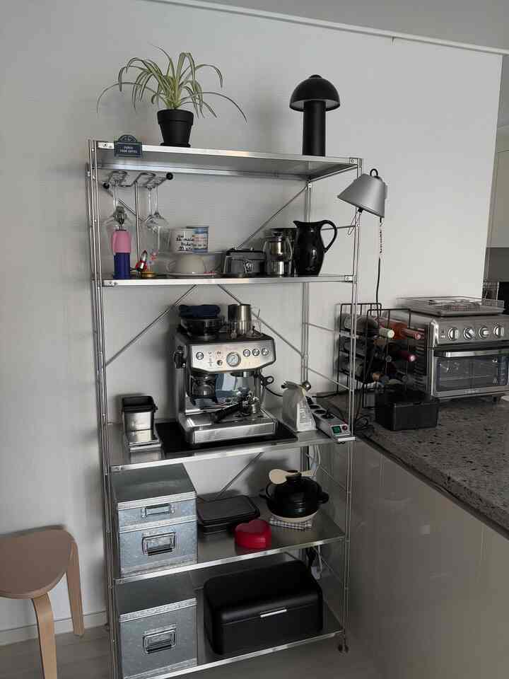 白い壁とメタル棚があるキッチンエリア、コーヒーマシンと整頓されたキッチン用品が配置された実用的なおうちカフェ空間
