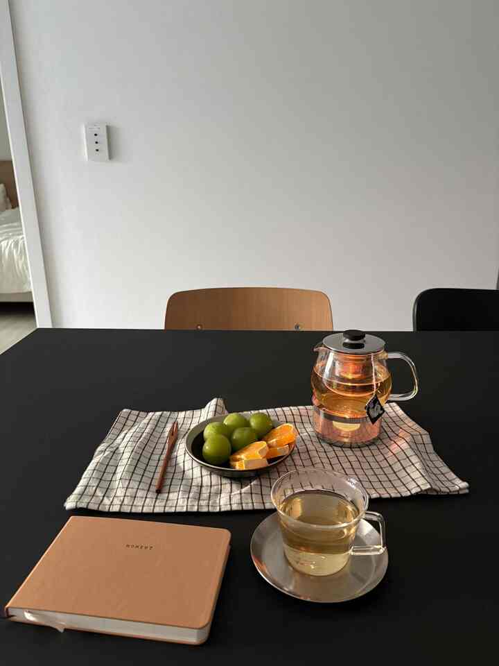 黒い天板のダイニングテーブルにティーポット、カップ、果物が置かれたシンプルな一人暮らしの空間