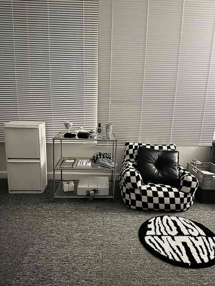 黒と白のトーンのリビングルーム、チェッカーボード柄のアームチェアとメタル棚、丸いラグが配置されたモダンで清潔感のある空間
