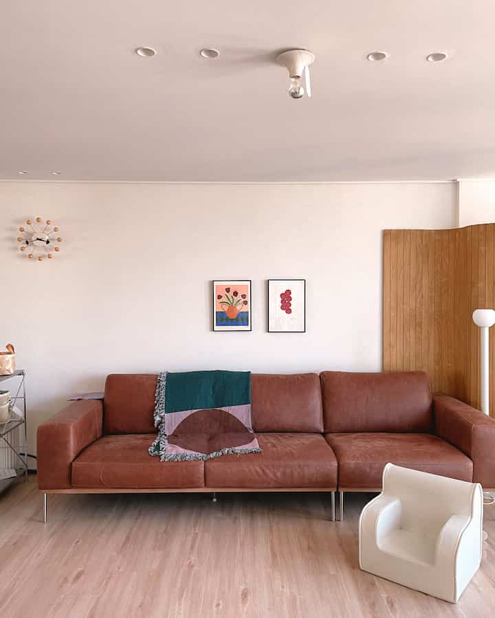 ナチュラルなブラウン調のリビング、ブラウンレザーのソファと木製の間仕切りが配置されたシンプルで落ち着いた雰囲気のインテリア