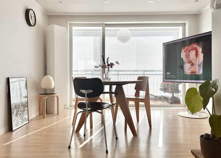 白い壁とナチュラルな木目調家具が配置された居心地の良いリビング、大きなベランダ窓とシンプルなダイニング空間を含む