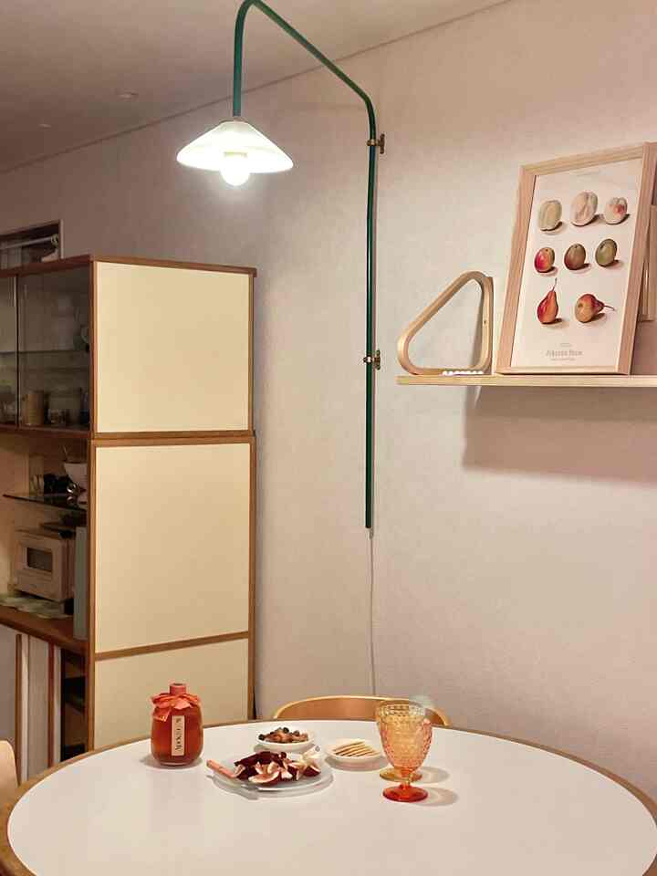 ナチュラルな色調の壁と木製家具が調和するリビング、円形の白いダイニングテーブルと棚、暖かな照明が演出する雰囲気のあるインテリア