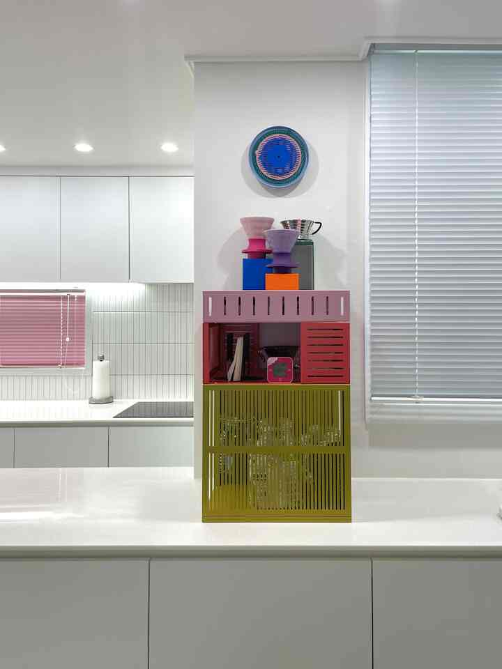 白い壁とキッチン用品のあるキッチン空間に、マルチカラーテサムマンス移動式収納ユニットと壁掛け時計が配置された清潔感のあるインテリア