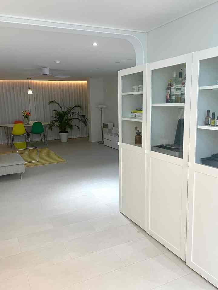 ホワイトでミニマルなトーンのリビングダイニング、ホワイトの本棚とカラフルなダイニングチェアが配された清潔感のある広い空間