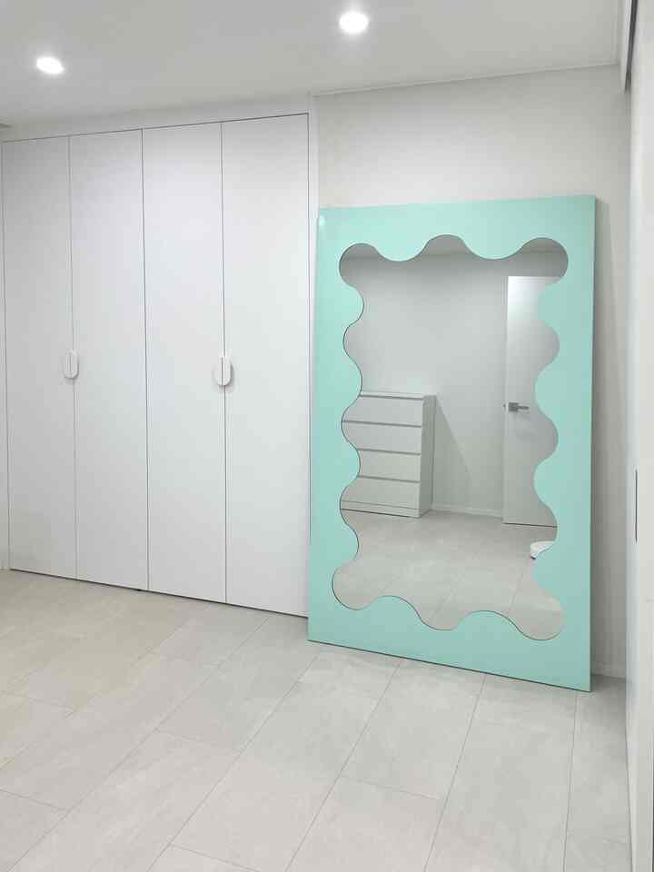 白とミント色のトーンのウォークインクローゼット、ビルトインクローゼットと波状の大型全身鏡が配置されたシンプルな空間