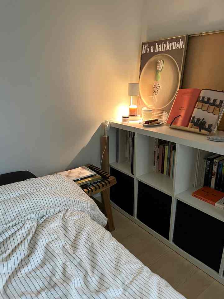 白と木目調が調和する一人暮らしの寝室、KALLAX本棚とスツール、キャンドルが落ち着いた雰囲気を演出する空間