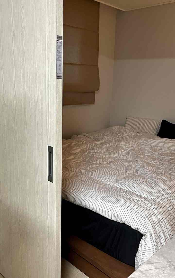 ナチュラルな色調の小さな寝室、引き戸と大きなベッドが配置された落ち着きのある空間