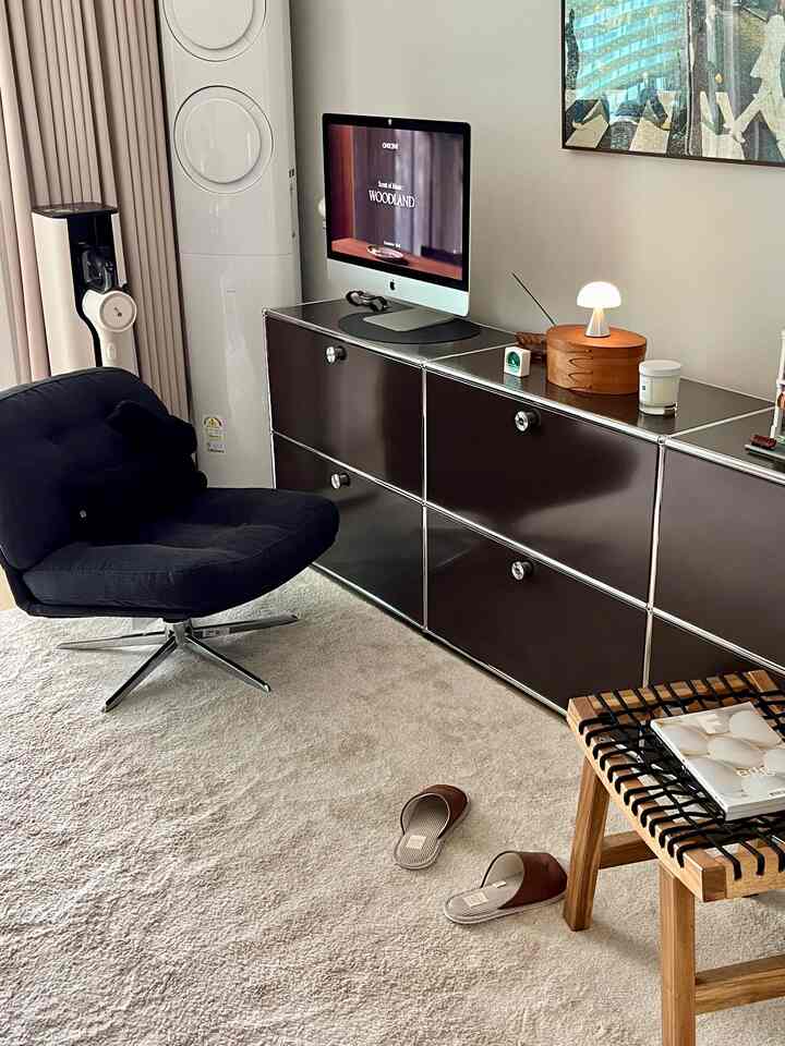 ナチュラルトーンの寝室ホームオフィス、ベージュのラグと黒のアームチェア、ダークメタリックの収納棚が配置された雰囲気のあるインテリア