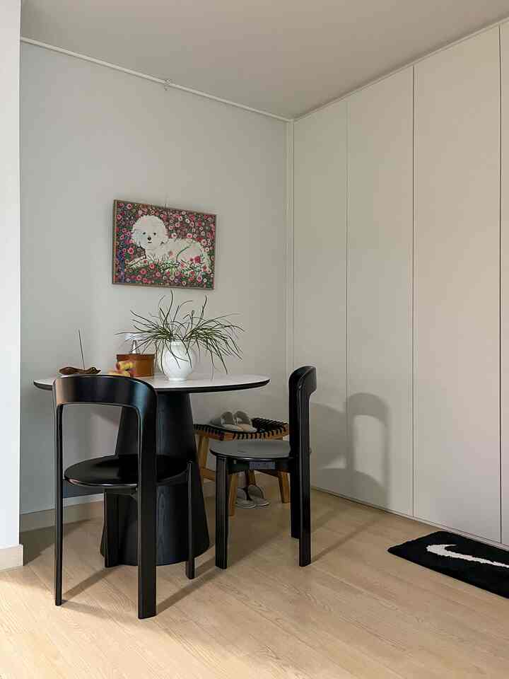 白い壁とナチュラルな木の床のコンパクトなリビングルームに、黒いダイニングテーブルと椅子、ペットの絵が飾られたモダンなインテリア