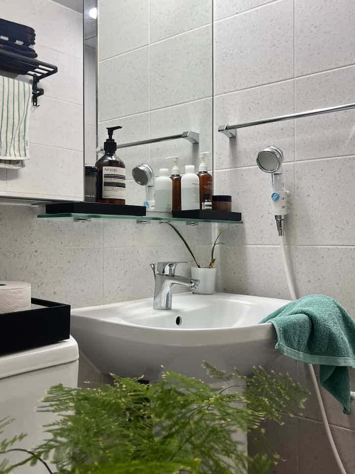 白と黒のトーンのバスルーム、中央に洗面台と鏡があり、タオル掛けやさまざまなバスルーム用品が配置された清潔感のある空間