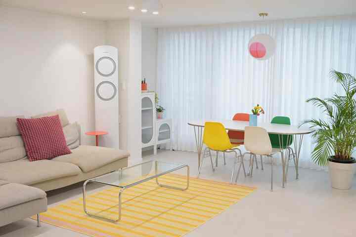 明るい白を基調としたリビングとダイニングの空間、ビビッドカラーのダイニングチェアと黄色のカーペットが配置された清潔感のあるインテリア