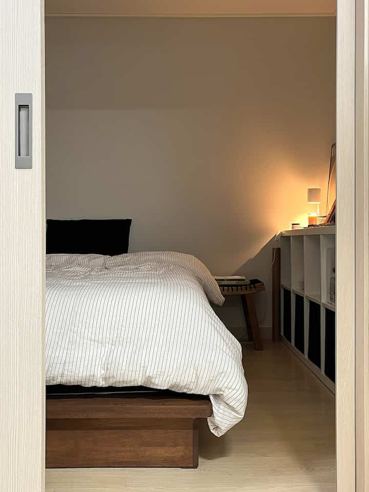 ナチュラルな茶色と白の色調の寝室、木製のベッドフレームと白い棚が配置された落ち着いた雰囲気のインテリア