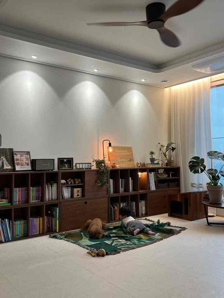 木目調家具と植物が配置されたリビング、緑のラグの上で赤ちゃんと犬がくつろぐ雰囲気のあるインテリア