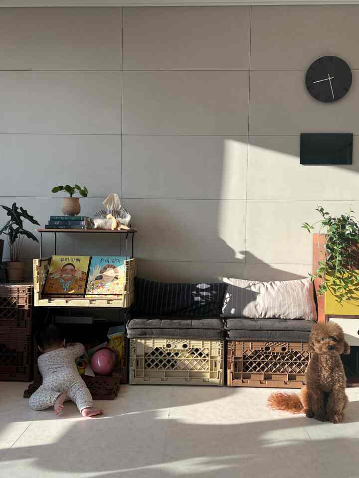 ナチュラルなベージュとブラウンのリビング、玩具収納とクッションが配置され、赤ちゃんと犬がいる落ち着いた雰囲気のインテリア