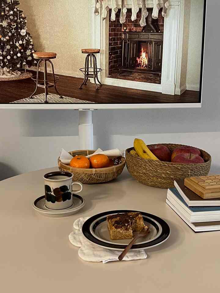 ホワイトトーンのキッチンスペース、中央にダイニングテーブルとフルーツバスケット、モニターが配置された落ち着いたホームオフィス兼用の雰囲気のある空間