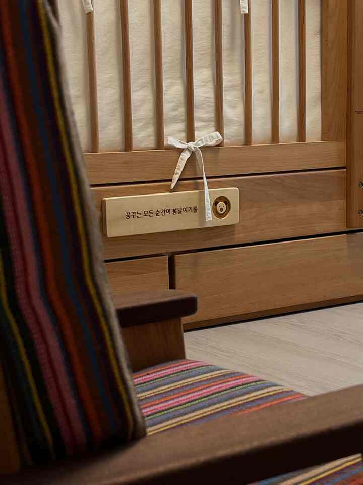 ナチュラルな色調のベビールーム、木製のベビーベッドとストライプ柄の木製アームチェアが配置された印象的な空間