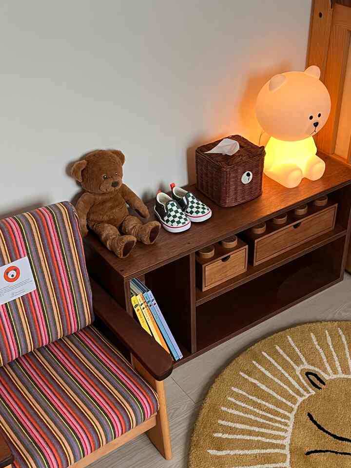 ナチュラルな木目調の子供部屋、テディベアとベビーシューズ、かわいいクマ型ランプが配置された温かみのある空間