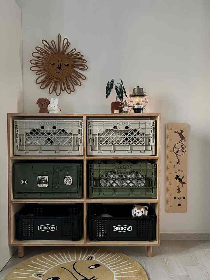 ナチュラル色調の子供部屋、木製収納棚に多彩な収納ボックスとライオンの顔のラグが配置された温かみのある空間