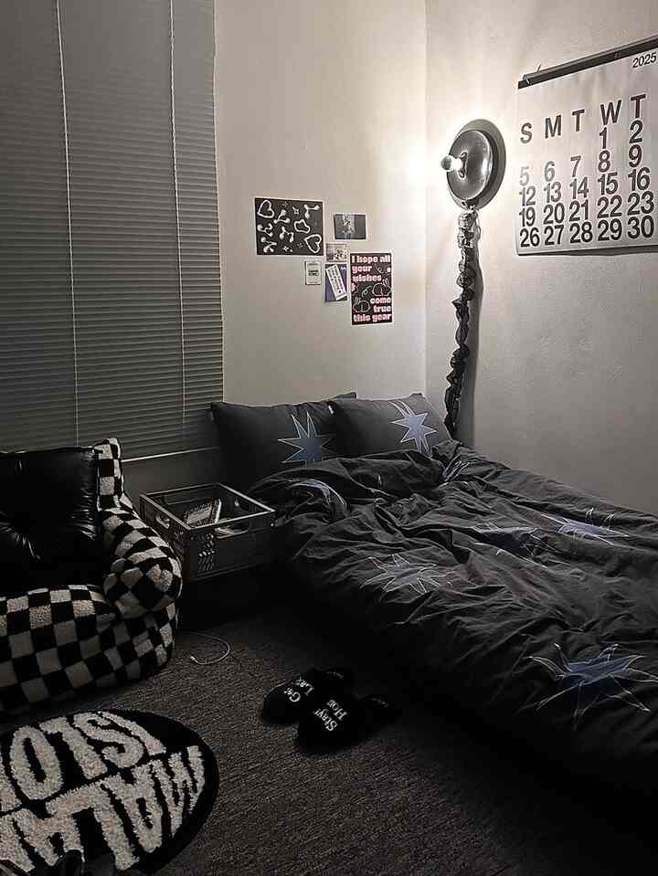 モノトーンの寝室空間、星柄の寝具とチェッカー柄のアームチェア、壁の照明とブラインドが配置された雰囲気のあるインテリア