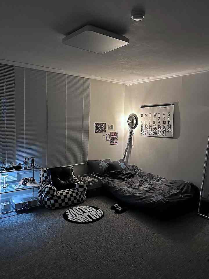 ブラックとグレーのトーンの寝室、ベッドとチェッカーパターンのアームチェア、ブラインドとブラケットライトが配置されたコンパクトな空間