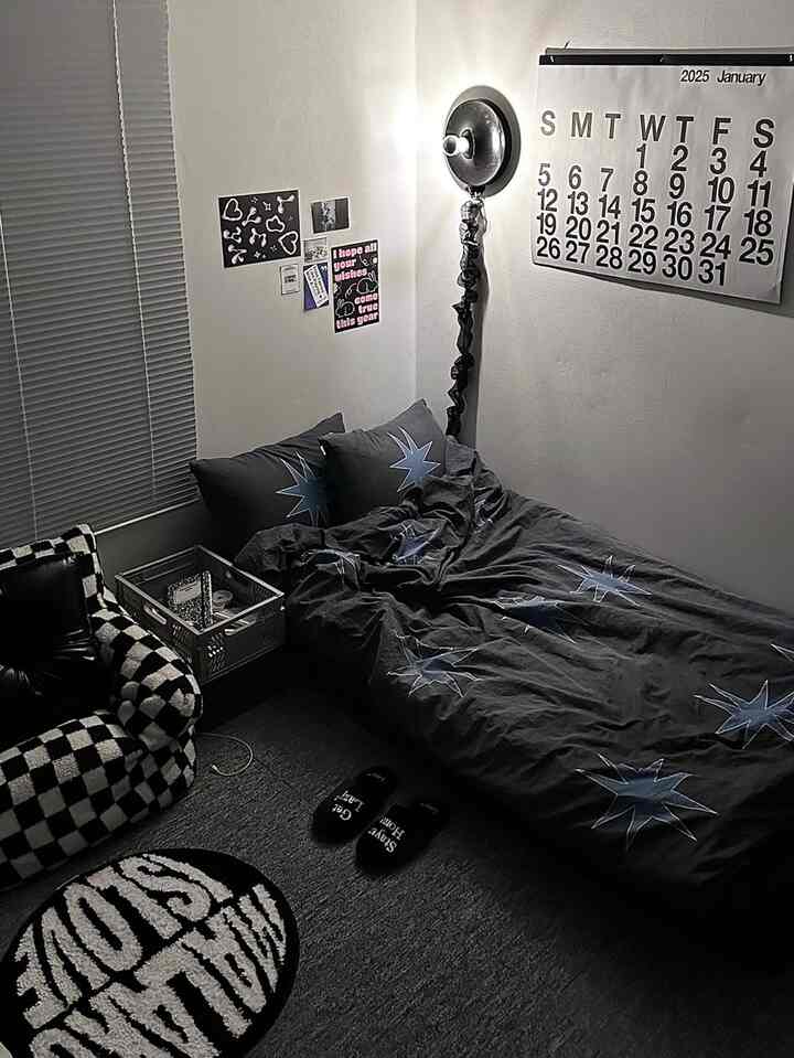 ブラックとグレーのトーンが特徴的なコンパクトな寝室、チェッカーパターンのアームチェアとシンプルな壁飾りが配置されたミニマルなインテリア