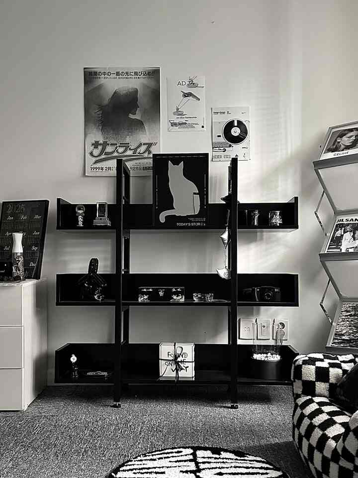 黒とモノトーンを基調としたリビング、中央に本棚と壁のポスター、右側にチェッカーパターンのソファが配置されたおしゃれな空間