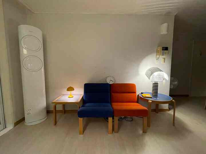 白い壁と床に青とオレンジのソファが配置されたシンプルなリビング空間、テーブルランプが雰囲気を演出