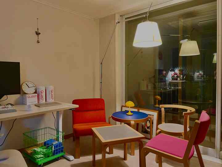 ナチュラルなベージュの壁と木製家具が配置されたリビング兼ホームオフィス、赤とピンクの椅子がアクセントとなっている雰囲気のあるインテリア