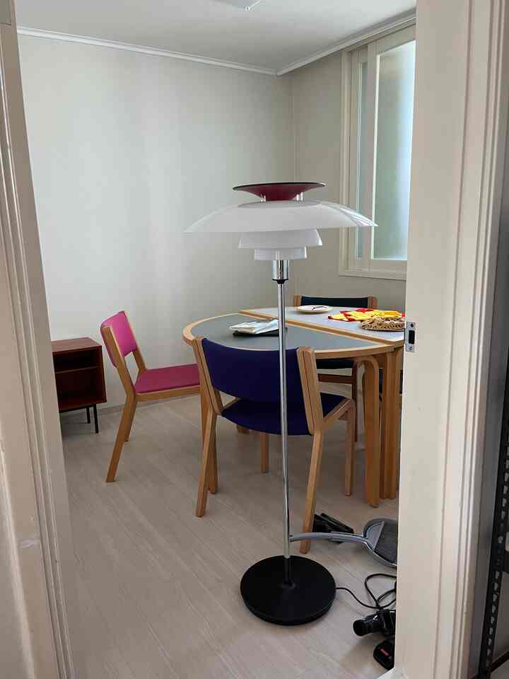 明るい木目調の床と白い壁のダイニングルーム、中央にフロアランプと木製のテーブルと椅子が配置されたシンプルでナチュラルな雰囲気の空間