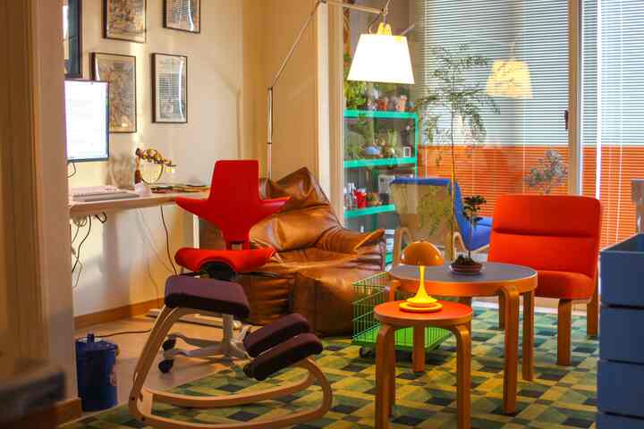 暖かいナチュラルな色調のコンパクトなホームオフィス、赤い椅子とブラウンのビーンバッグ、緑のラグと植物が配置された雰囲気のあるインテリア