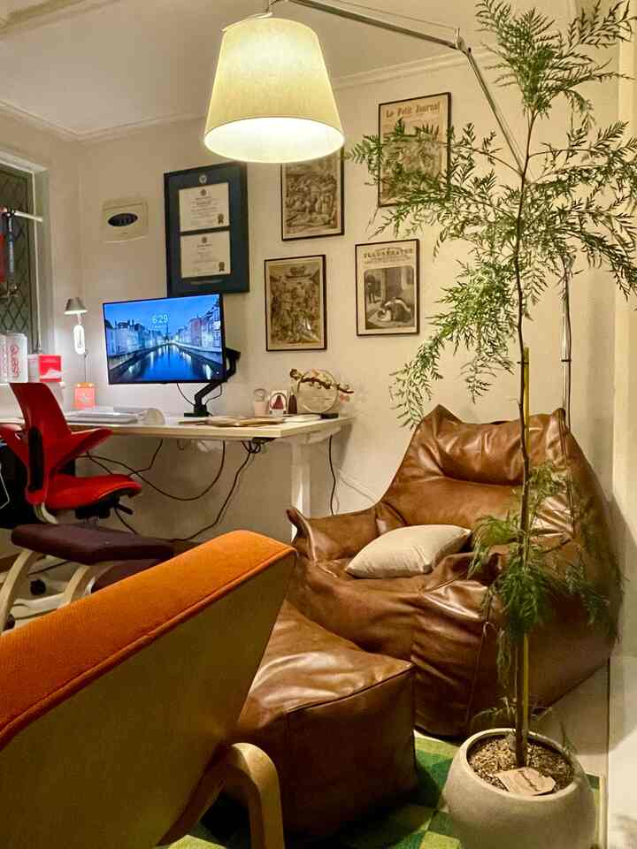 白い壁と茶色のビーズクッションソファ、赤いオフィスチェアが配置されたモダンなホームオフィスのインテリア