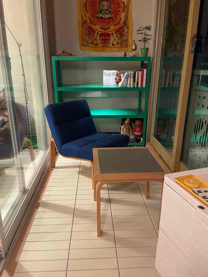 木目調の床とブルーのアームチェアがあるコンパクトなバルコニー、グリーンの収納ラックが配置された落ち着いた空間