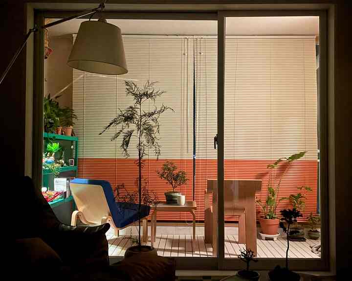 暖かいオレンジ色と木目調が調和したバルコニー、青いクッション付きアームチェアと植物が配置された落ち着いた空間