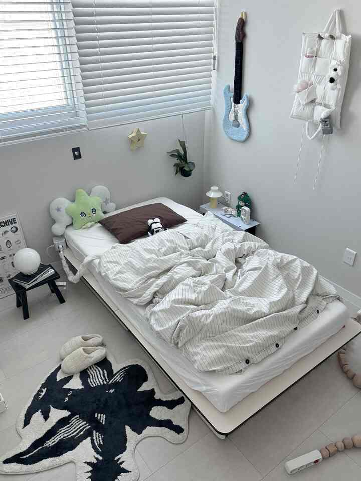 ホワイトとグレーの色調の小さな寝室、シンプルなベッドとかわいい小物が配置されたミニマルな空間