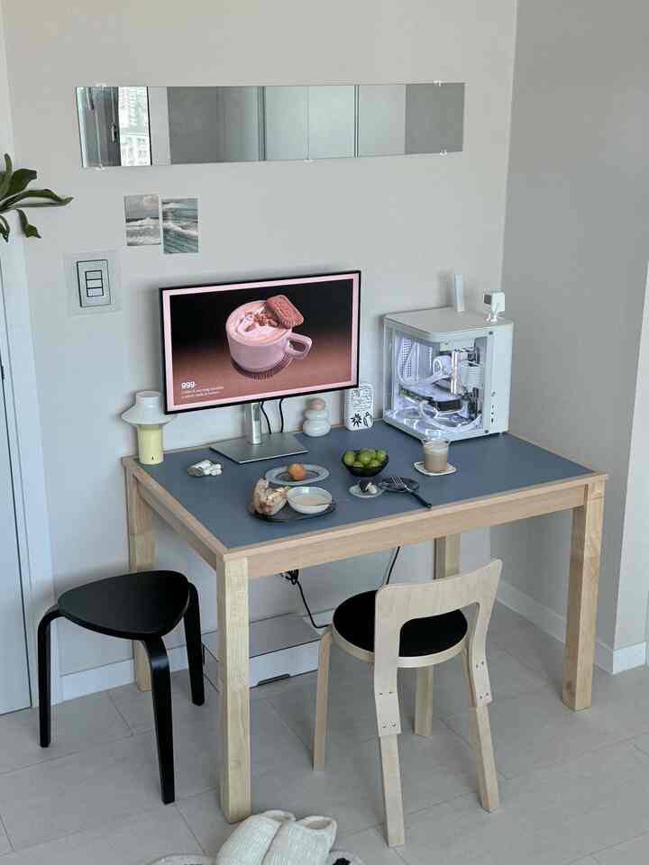 白い壁と木目調のダイニングテーブルが配置されたシンプルなおうちカフェ空間、テーブルの上にモニターとコーヒー用品が置かれている