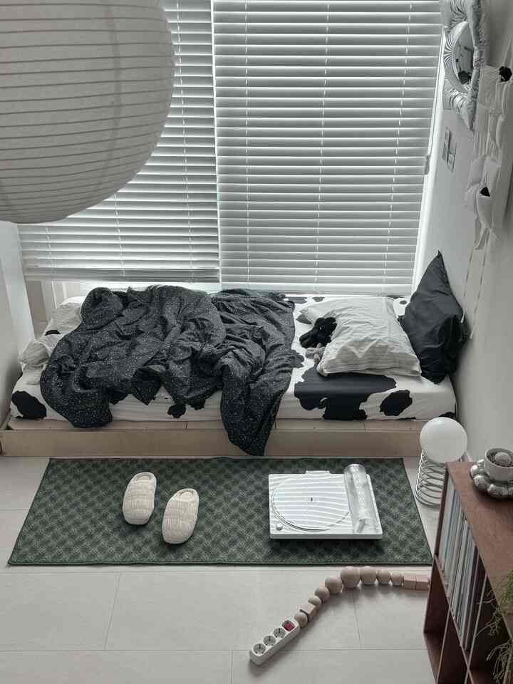 ホワイトとウッドトーンのコンパクトな寝室、ブラインド付きの窓とベッド、グリーンのラグがある雰囲気の良い空間