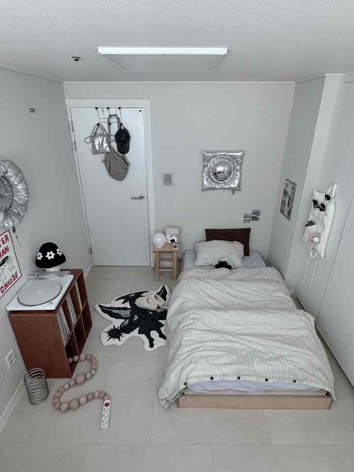 明るい白とグレーのトーンの一人部屋寝室、ベッドとクローゼット、ターンテーブルとスツールが配置されたモダンな空間