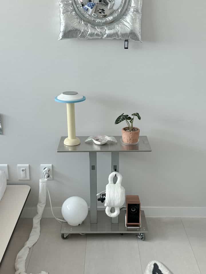 シルバーとホワイトのトーンの寝室、ステンレス製サイドトロリーのナイトテーブルとアクセサリーが配置された落ち着いたモダンなインテリア